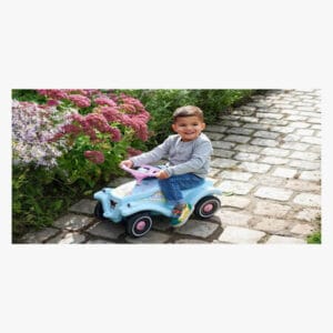 Pieni lapsi ajaa potkuautolla mukulakivikadulla kukkien vieressä