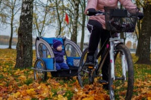 Lapsi istuu pyöräkärryssä aikuisen pyöräillessä syksyisessä puistossa