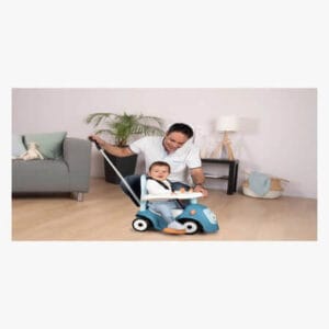 Aikuinen työntää lasta potkuautossa työntötangon avulla sisätiloissa