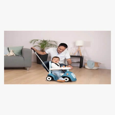 Aikuinen työntää lasta potkuautossa työntötangon avulla sisätiloissa