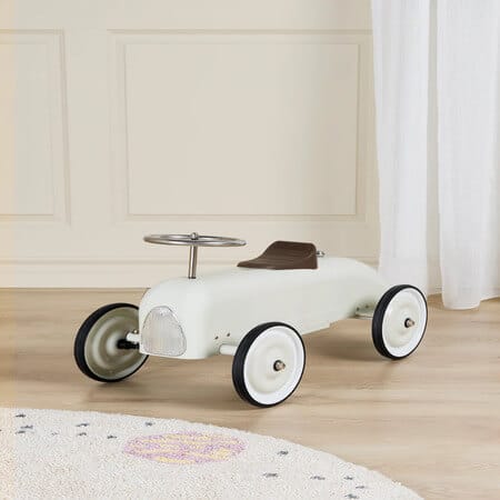 Valkoinen retrohenkinen potkuauto lapselle sisätiloissa puulattialla