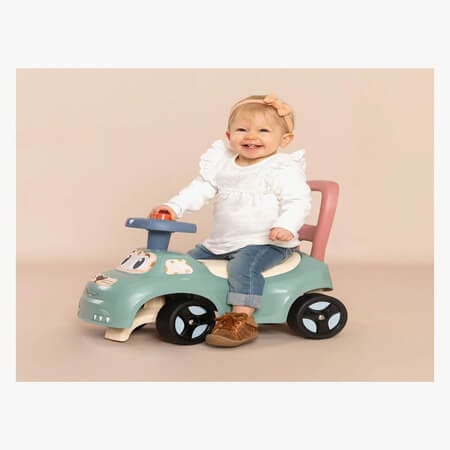 Vauva istuu potkuautossa sisätiloissa ja hymyilee kameralle