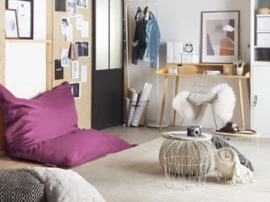 Violetti säkkituoli modernissa nuortenhuoneessa, jossa on työpöytä, metallituoli, seinäkuvia ja pieniä sivupöytiä.